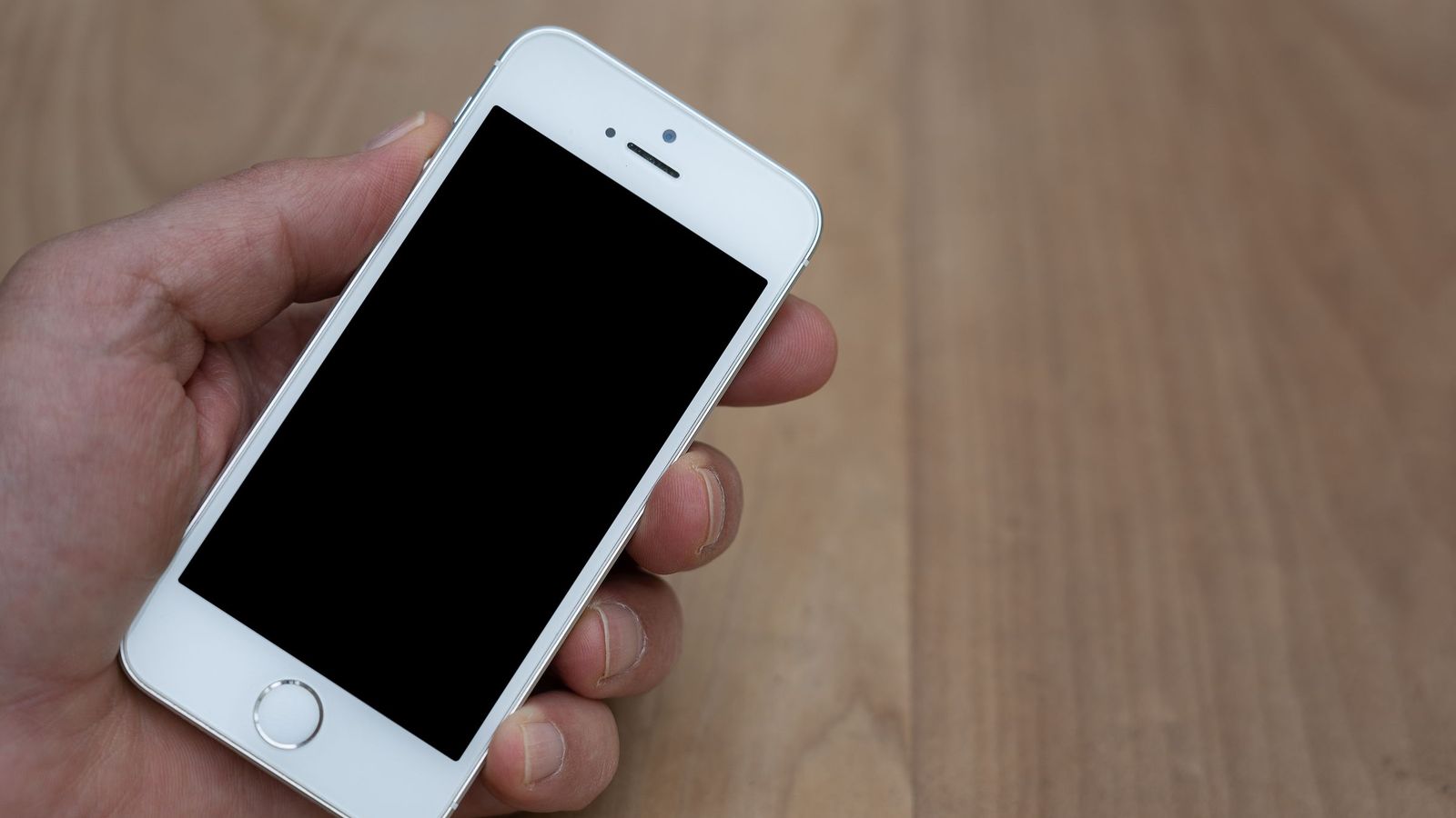 Une main tient un smartphone au-dessus d'une table en bois.